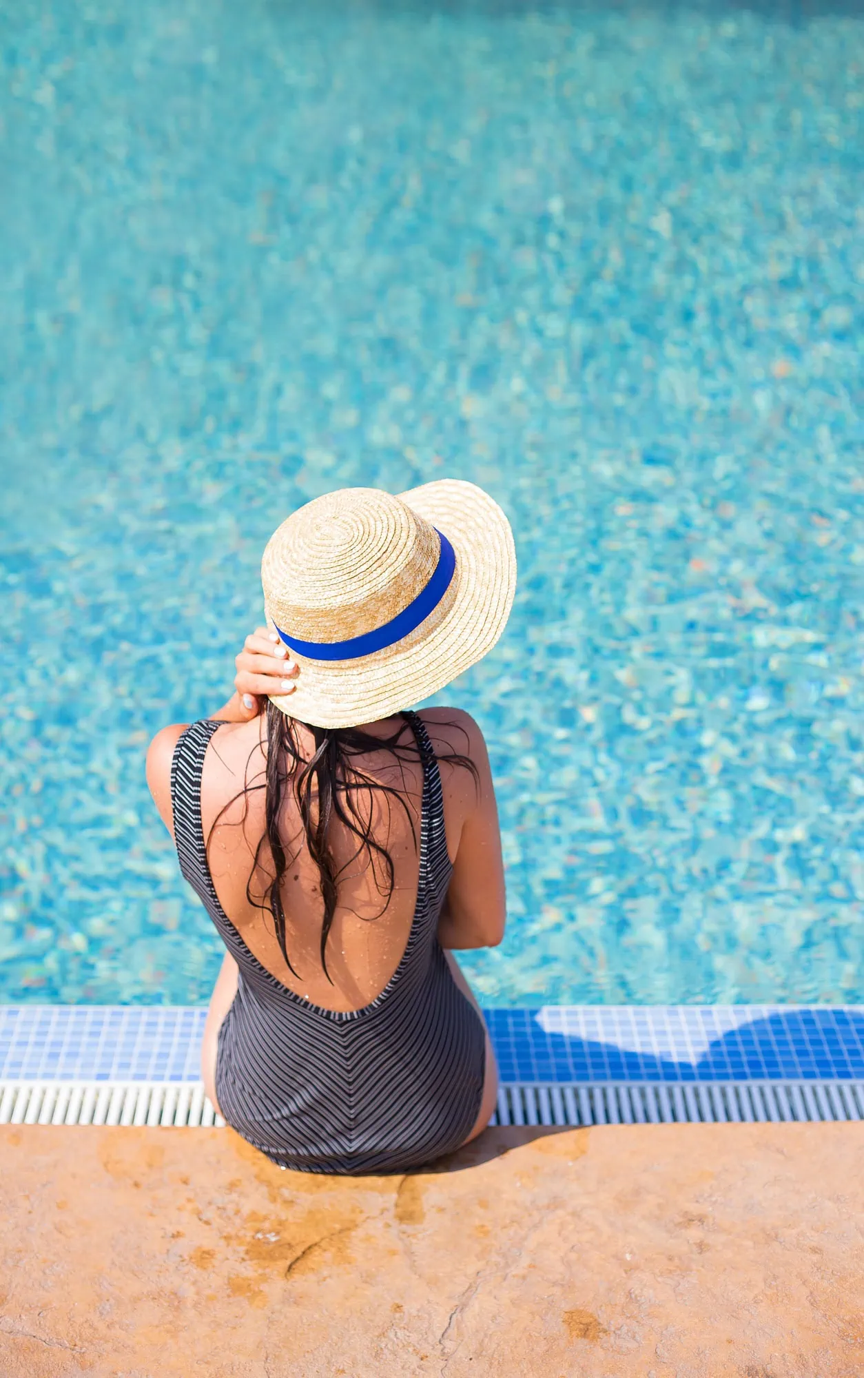 Beautiful girl in a black swimsuit near a blue pool