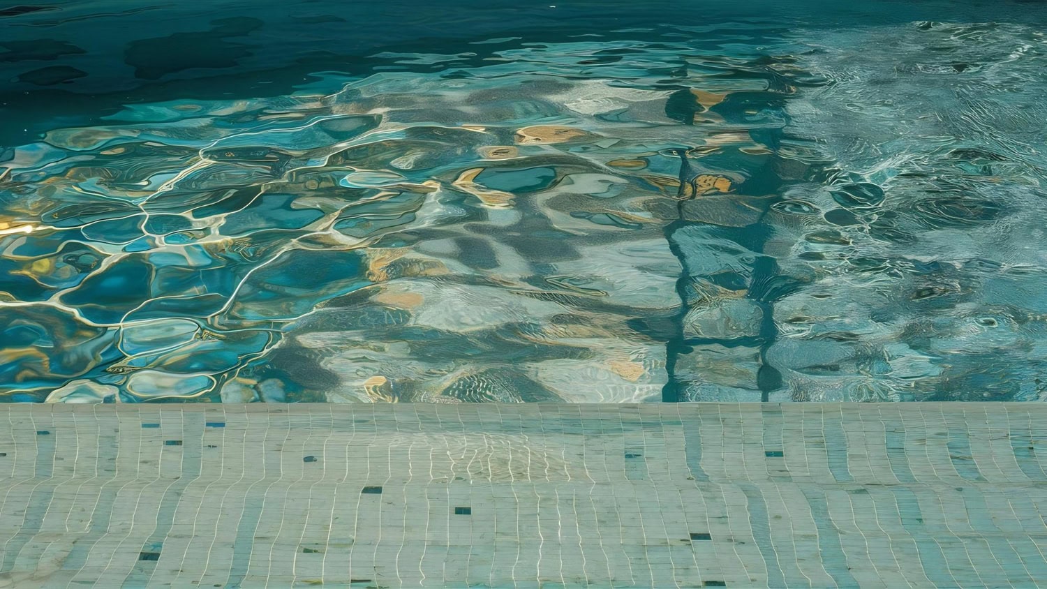Close-up of a swimming pool with clear blue water, ripples casting reflections, and tiled steps partially submerged in the bottom right corner—a perfect result after proper pool water cleaning to fix cloudy pool issues.