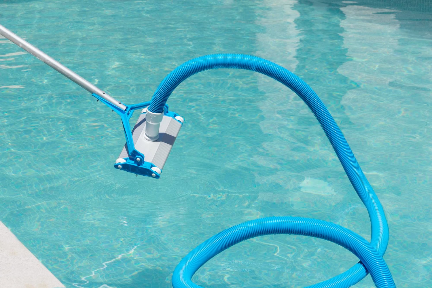 A manual pool vacuum with a blue hose and handle is submerged in a swimming pool, providing deep pool cleaning as it tidies the pool floor.