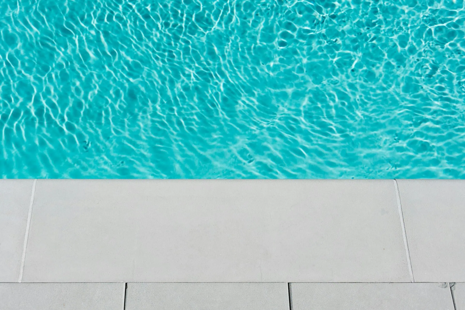 A view of clear blue water in a swimming pool with light-colored tiles along the pool edge, perfect for enjoying summer days in Corpus Christi.